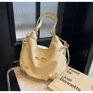 Detail of cream pleated leather tote featuring bow accents and elegant ribbon straps