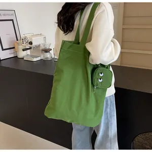 Detailed view of green canvas tote bag with embroidered cartoon monster coin purse charm