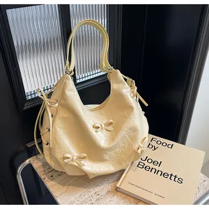 Detail of light yellow pleated hobo bag featuring decorative bows and silver eyelets
