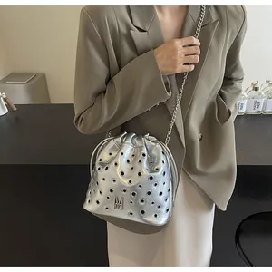 Détail du sac seau argenté avec œillets et logo M métallique sur un tailleur