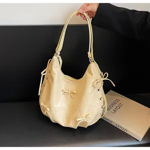 Close-up of cream hobo bag featuring decorative bows and wrinkled PU leather texture