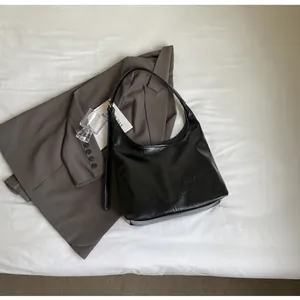 Sac hobo noir en cuir huilé ciré posé sur un drap blanc de style minimaliste