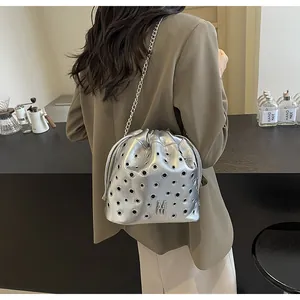Détail du sac seau métallisé argenté avec œillets et bandoulière chaîne sur modèle