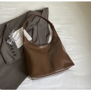 Détail du sac hobo en cuir plissé marron foncé posé sur un drap blanc avec magazine