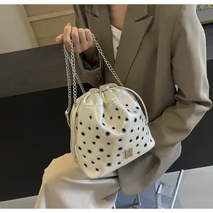 Détail du sac seau blanc cassé avec œillets argentés et bandoulière chaîne sur mannequin