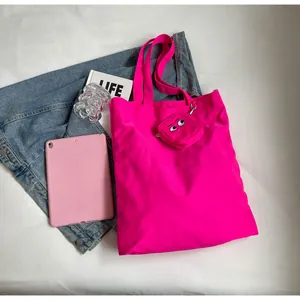 Hot pink nylon tote bag with cartoon eye charm shown in an urban lifestyle flatlay setup