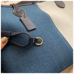 Gros plan du sac fourre-tout en denim avec surpiqûres blanches et anneaux en métal doré