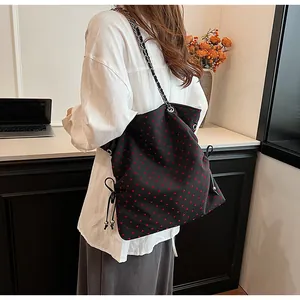 Detail of black tote bag featuring red heart patterns and silver chain shoulder straps