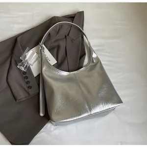 Détail du sac hobo métallisé argenté avec texture plissée sur fond de costume marron chic