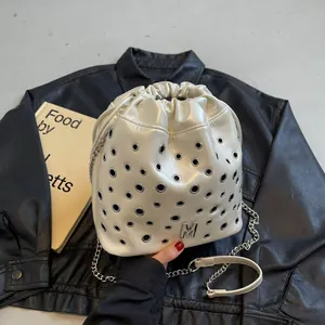 Sac seau ivoire avec œillets argentés et lettre M en métal sur fond noir