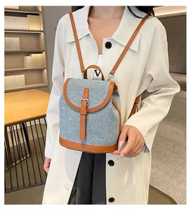 Detail shot of light blue denim and brown leather backpack with silver buckle on a model
