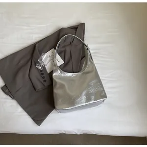 Détail du sac hobo argenté métallisé avec texture plissée sur fond de costume gris