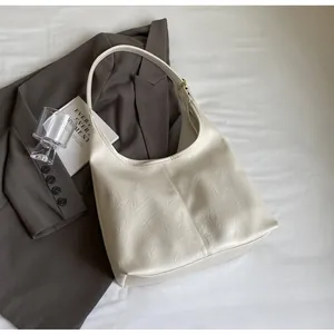 Détail d'un sac hobo crème à texture plissée posé sur un blazer gris chic