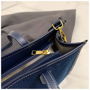 Detailed view of dark blue denim tote bag with contrast stitching and gold zipper