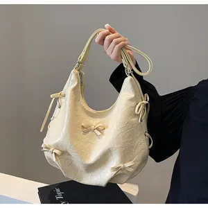 Detailed macro view of the cream hobo bag showing pleated texture and 3D bow accents