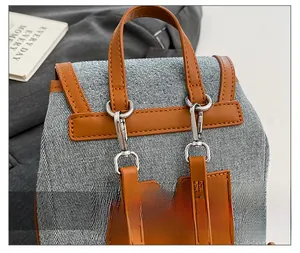 Detail of the gray denim backpack showing brown leather handle and silver metal hardware