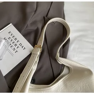 Détail macro du cuir plissé blanc cassé et de la boucle dorée de ce sac à bandoulière