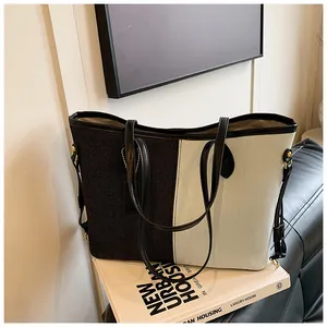 Détail du sac cabas en denim bicolore avec bandoulière noire et détails dorés