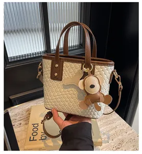 Detail of woven beige tote bag featuring brown leather trim and cute monkey charm accessory