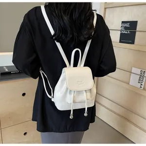 Detail view of small white faux leather backpack with drawstring closure and metal charms