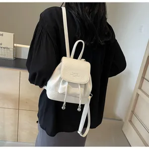 White pebbled leather mini backpack shown from back view on model with drawstring closure