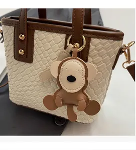 Detail of woven tote bag featuring brown leather trim and a cute monkey bag charm decoration