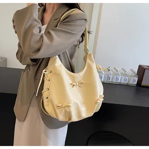 Detail of light yellow hobo bag featuring decorative bows and side drawstring details