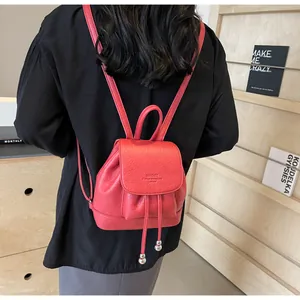 Rear view of a red mini leather backpack with drawstring closure and flap on a model