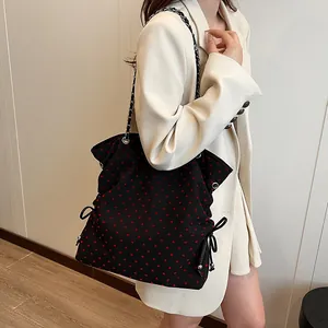 Black tote bag with red heart pattern and chain strap worn by a model in a suit