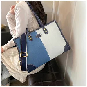 Detail view of large color-block denim tote bag with leather trim and wide shoulder strap