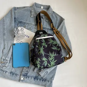 Top view of black crossbody chest bag with green leaf pattern on denim jacket
