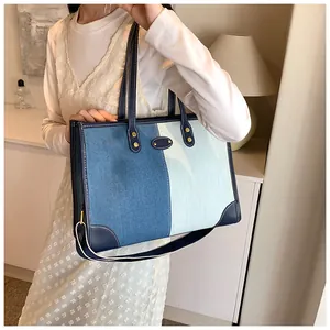 Detail of two-tone denim tote bag with leather trim and gold rivet accents on model