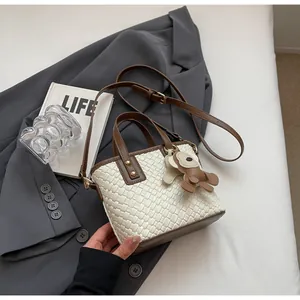 Detail of woven leather tote bag with brown trim and small bear keychain ornament
