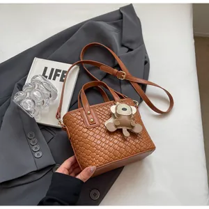 Detail of woven texture tote bag in caramel brown with monkey charm and shoulder strap