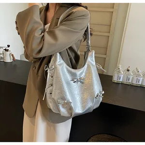 Detail of silver metallic tote bag featuring bow accents and pleated texture on model