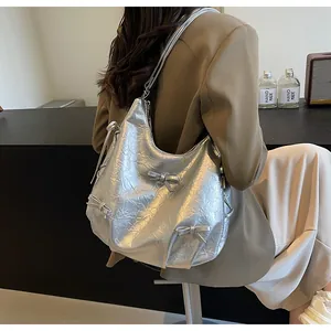 Detail of silver pleated shoulder bag with metallic finish and bow accents worn by model