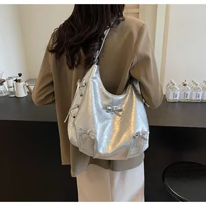 Silver metallic tote bag with bow detail and crinkled leather texture on model shoulder