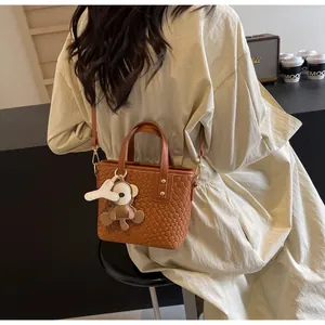 Rear view of model wearing brown woven tote bag with cute bear charm and shoulder strap