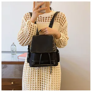 Detail of a black nylon backpack with flap closure and silver hardware on a model