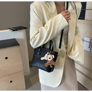 Detail of black woven texture tote bag with a cute monkey charm and leather shoulder strap