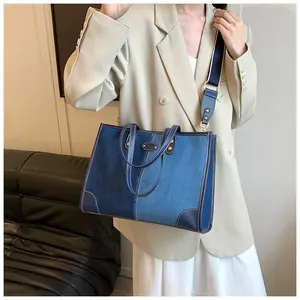 Detail of blue denim tote bag with leather trim and adjustable shoulder strap on model