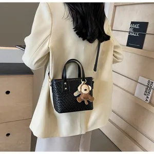 Detail of black woven texture tote bag with a cute bear pendant on a shoulder strap