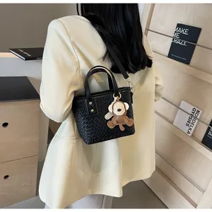 Detail of black woven texture tote bag with a small monkey charm on a beige suit