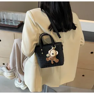 Detail of a black woven tote bag with a leather strap and a cute bear charm on a model