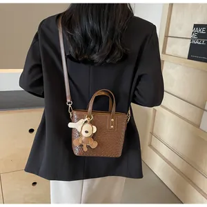 Detail of dark brown woven texture leather tote bag with cute yellow bear pendant
