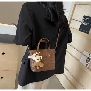 Brown woven tote bag with cute monkey charm shown on shoulder with a black blazer