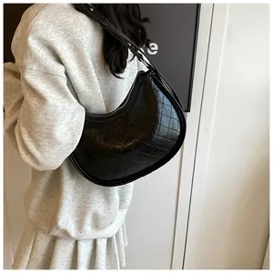 Quilted black underarm crescent bag with glossy finish shown on model in a casual outfit