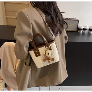 Detail view of woven white handbag with brown leather straps and a cute plush charm