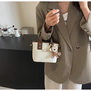 Detail of cream woven tote bag featuring brown leather trim and a small monkey pendant