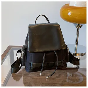 Detail of contrast textures on black backpack showing matte fabric and glossy leather lid